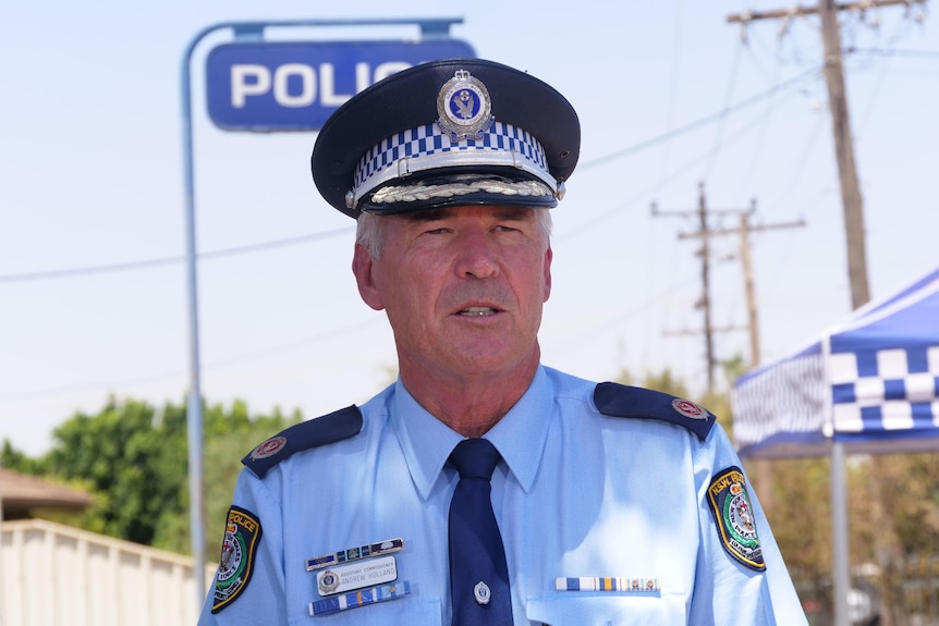 Senior police officer in uniform stands in front of a police sign.