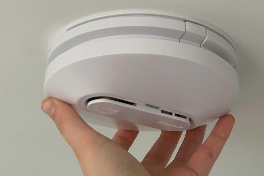white smoke alarm with hand touching it