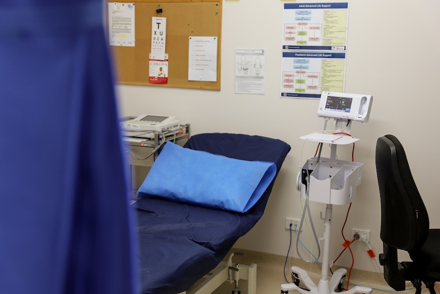 A room with medical equipment and a bed covered in a dark blue sheet, there are posters on the wall.r in the b