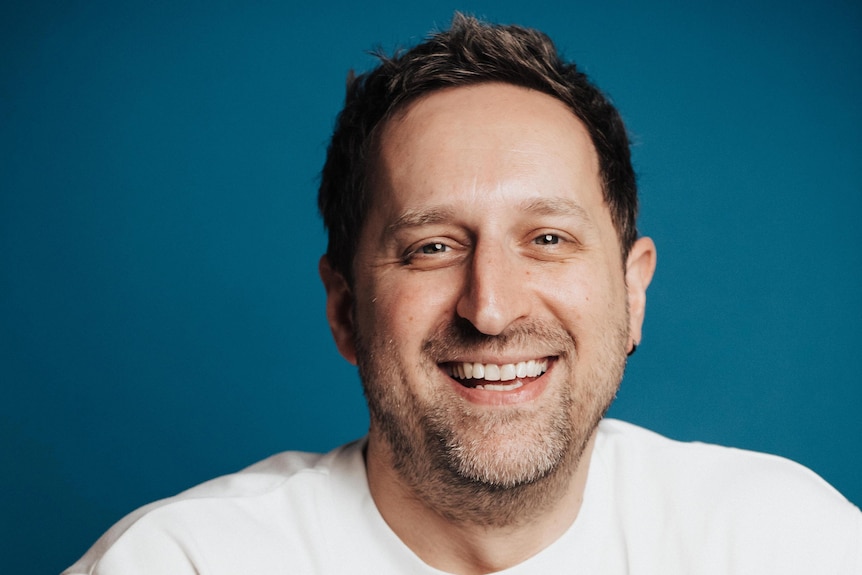 A headshot of a man wearing a white t-shirt.