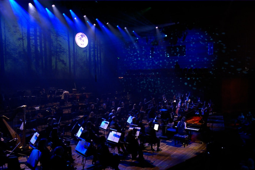 Melbourne Symphony Orchestra on stage with Andrea Lam at the piano. There are forest projections in the hall with a full moon.
