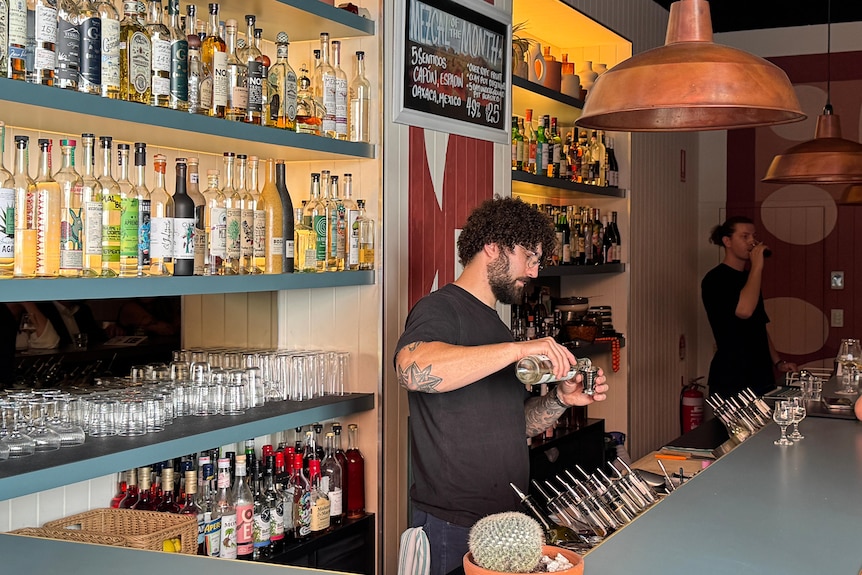 A man working behind a bar with spirits behind him.