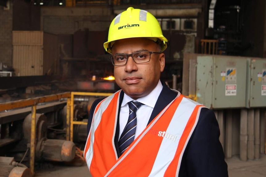 Sanjeev Gupta in a hard hat with a steelworks production line behind him.