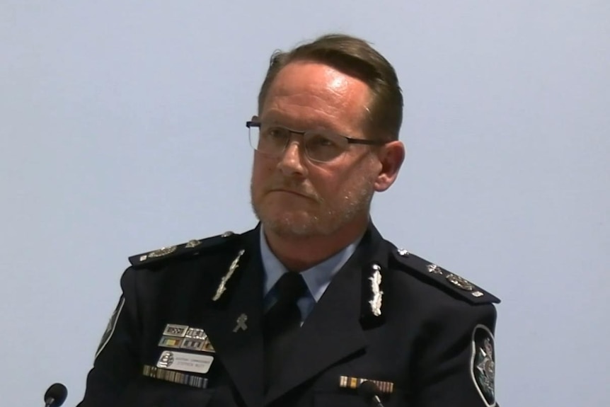 Man in police uniform sits behind microphone, grey background