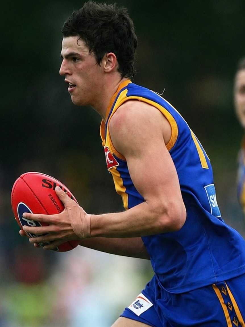 A footballer with a blue and gold jumper runs with the ball during a match.