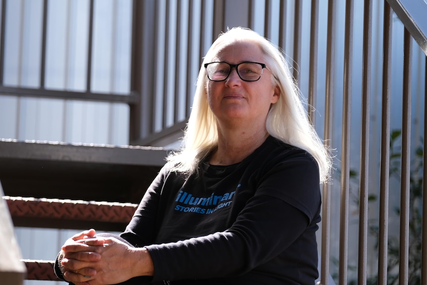 Cindi Drennan sits on the steps of some greying, metal stairs.