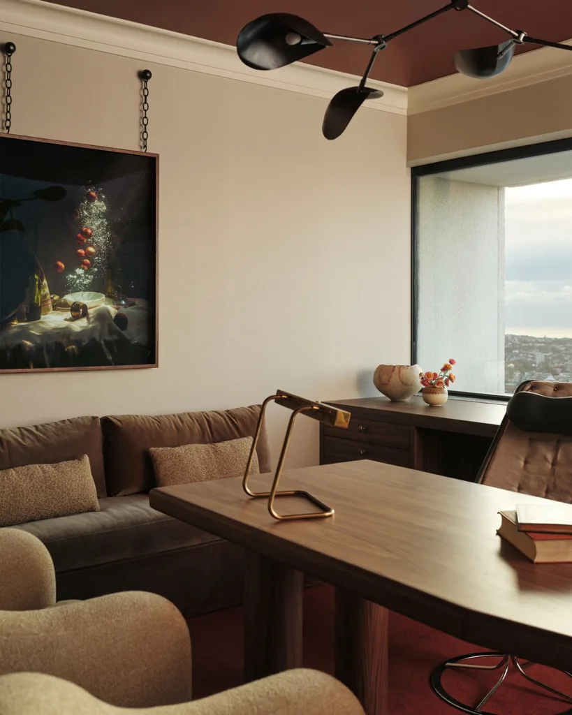 A daybed in velvet cushion opposing timber desk, leather armchair and city views