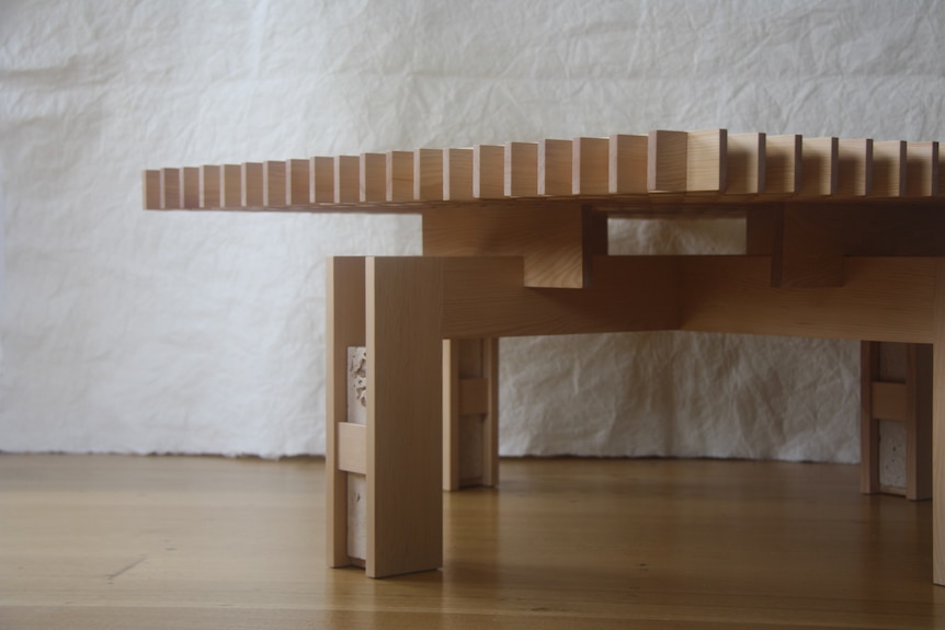 A low blonde wood table with a grid top and squat legs that extend beyond the table edges.