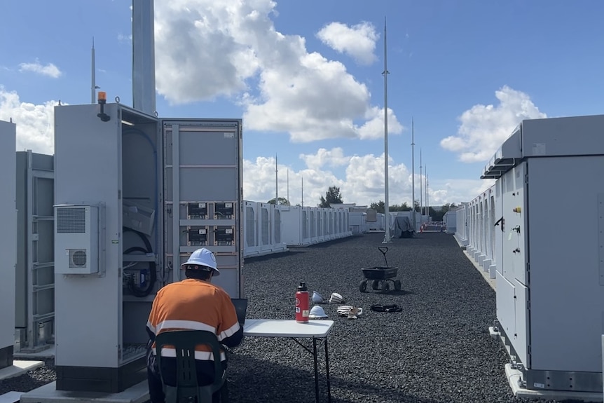 A worker in high-vis sits in front of a grid-scale battery.