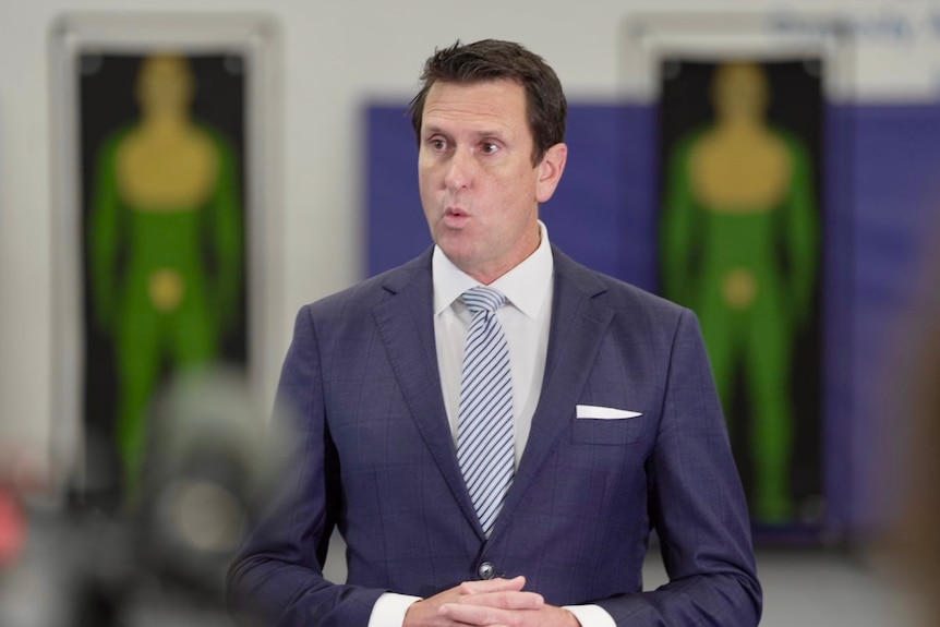 A man in a suit speaking in front of two human-shaped targets.
