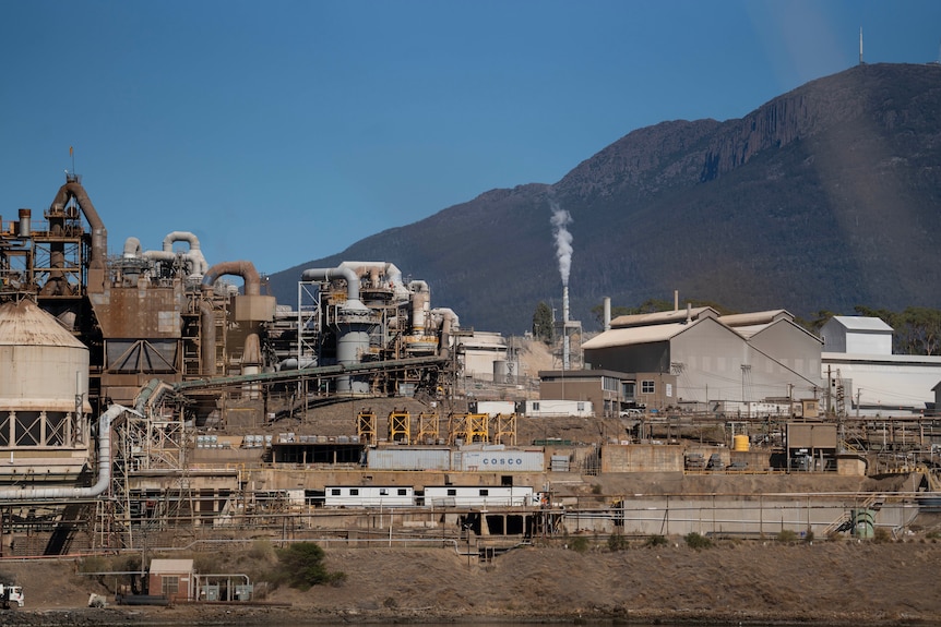 An industrial site on the bank of a river. A mountain range looms behind hit.