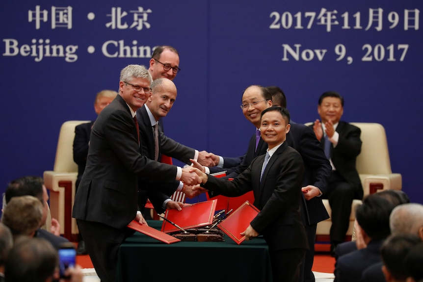 Men holding red folders shake hands over a long table.