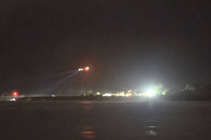 Distant picture showing helicopter hovering in dark with searchlight.