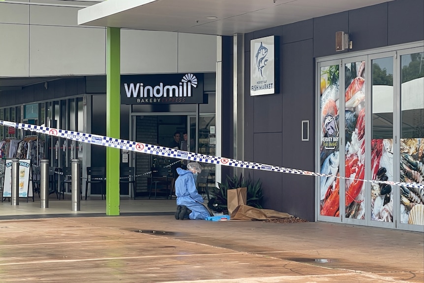 A police forensics officer kneels down at the scene of an alleged armed robbery.