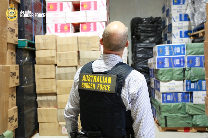 A man in an Australian Border Force union looks at stacked boxes in a shed.