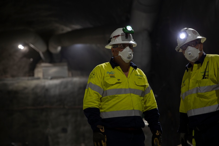 Two workers in construction outfits, in an underground tunnel.