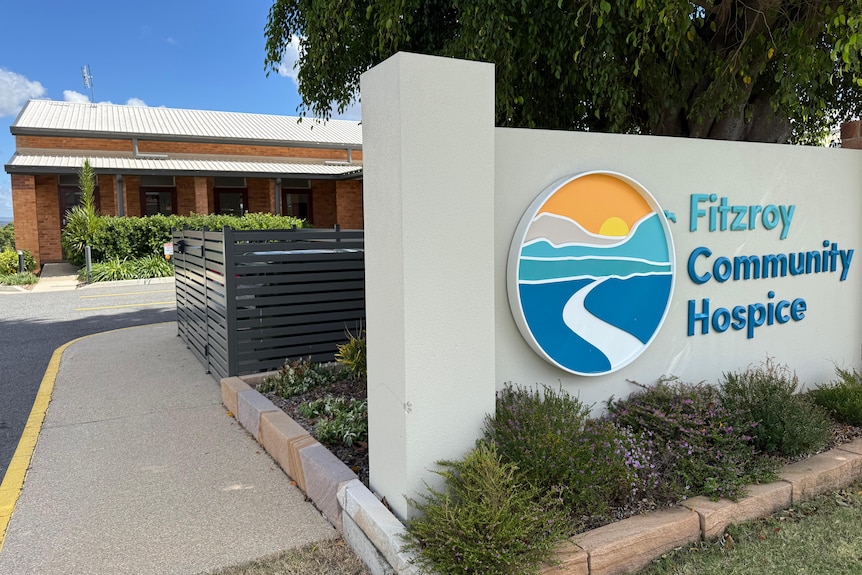 A light blue sign that says 'Fitzroy Community Hospice' is set against a grey wall in front of a brick building.