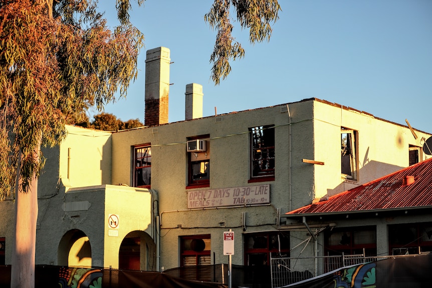 Sun shines on a pale blue coloured business, the windows are missing and hoarding sign fallen down. 