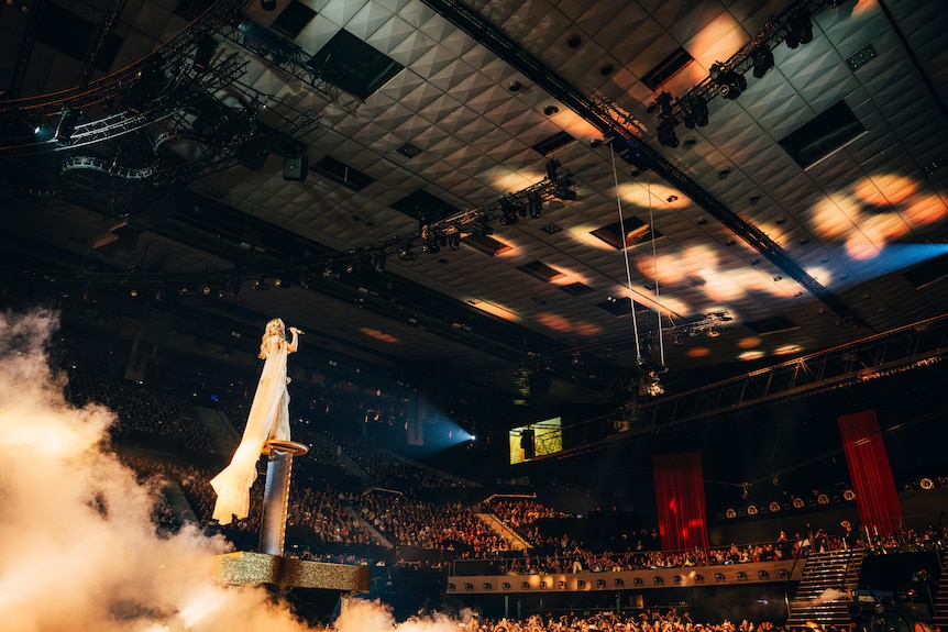 A female performer in a sparkly dress on an elevated platform on stage
