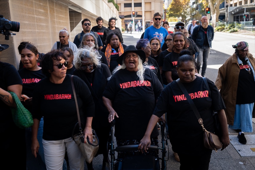 A group of Indigenous people wear black shirts emblazoned with the word 'Yindjibarndi'