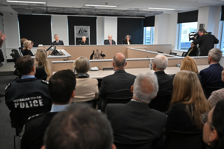 A group of men and women sit at the front of a room behind a large committee table.