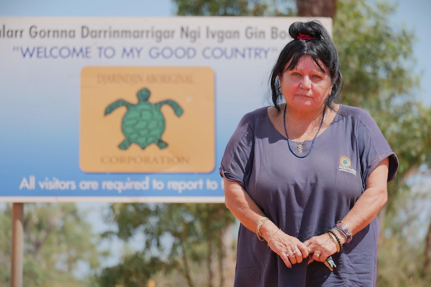 Woman in navy shirt and black hair tied in a bun standing infront of blurred community sign