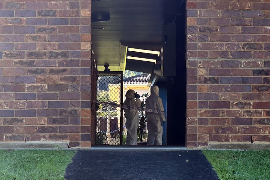 Police in white cover-all suits stand in a passageway between units