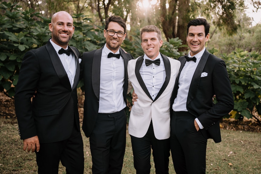 Four men in formalwear smile to the camera, Steven Mattaboni is in a white tux and the others are in black.