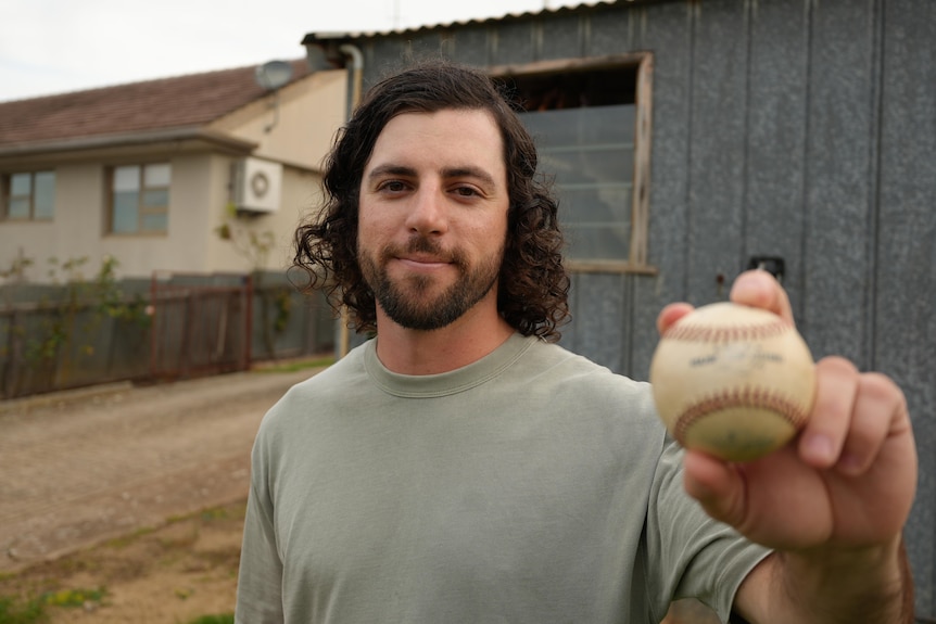 A man holds a baseball up to the camera. The baseball is blurred.