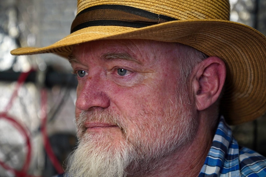 A close-up portait of an older white man with a white beard and wearing a straw hat.