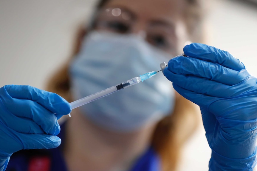 A woman holds up a needle next to a vial.
