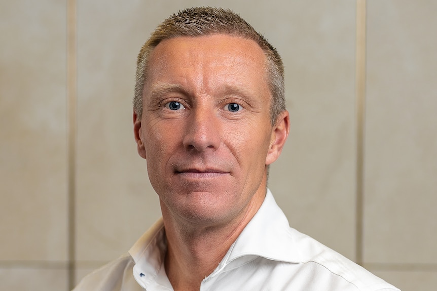 A middle-aged man wearing a white button-up looking into the camera.
