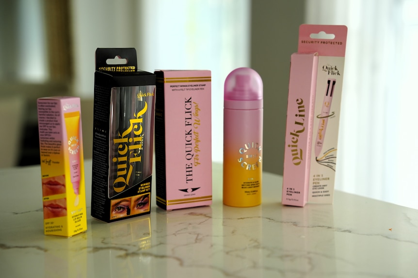 Six packaged products - in pink, one is black, packagine, on a marble counter top.