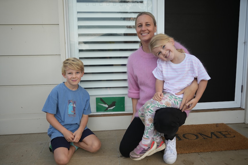 Spencer, Laura and Harper pose next to a green wagtail painting on a front doortstep.
