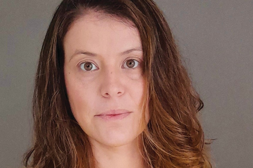 A brunette woman wearing a yellow shirt looking into the camera.