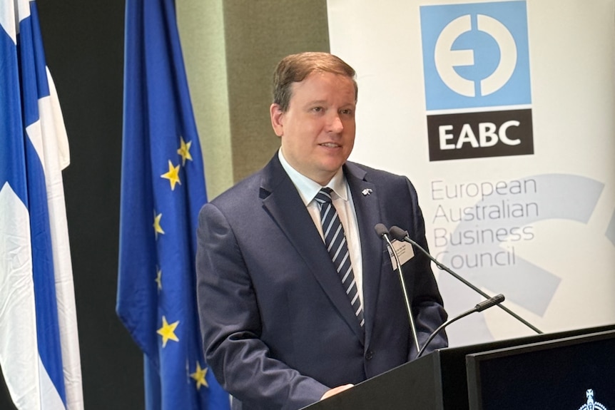 Finland's Trade Minister Ville Tavio standing in front of a dias, infront of European Australian Business Council banner.