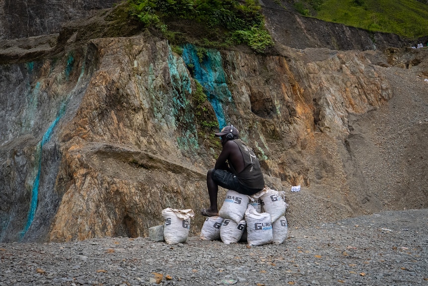 A mine worker sitting on bags looking to the side with a stained blue rock backdrop.