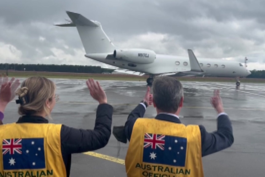 Two people wave to people on board as the plane is about to take off.