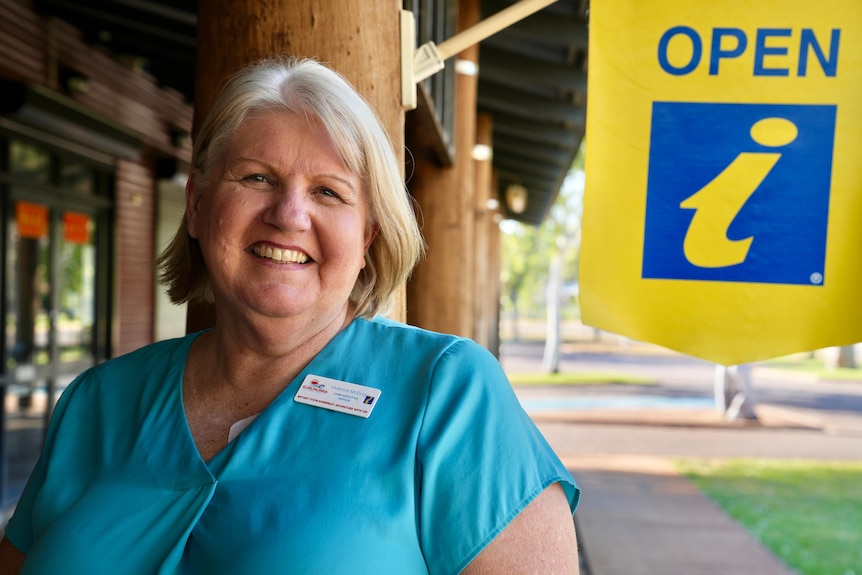 A blonde woman with posing next to an information sign.