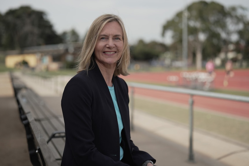 A woman is smiling, sitting on a bench at an athletics track.