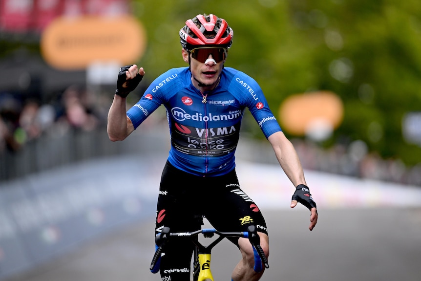 A cyclist clenches his fist as he rolls down a road in front of a crowd.