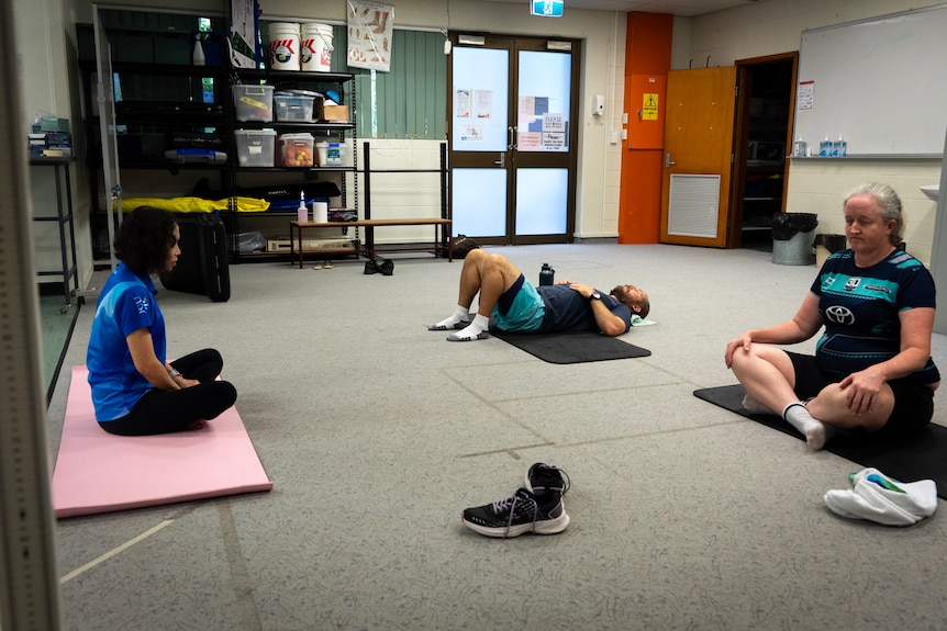 Three people meditate in a room - two women sit and a man lays down.