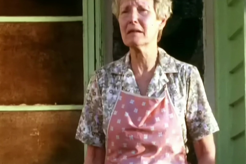 A woman stands with a distressed expression on her face.