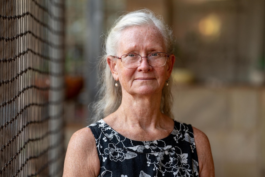 An older, silver-haired woman in glasses and a dark-coloured floral dress.
