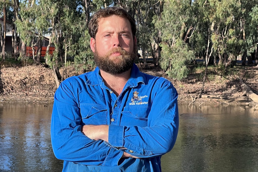 Bearded man in blue work shirt standing on the banks of a river.