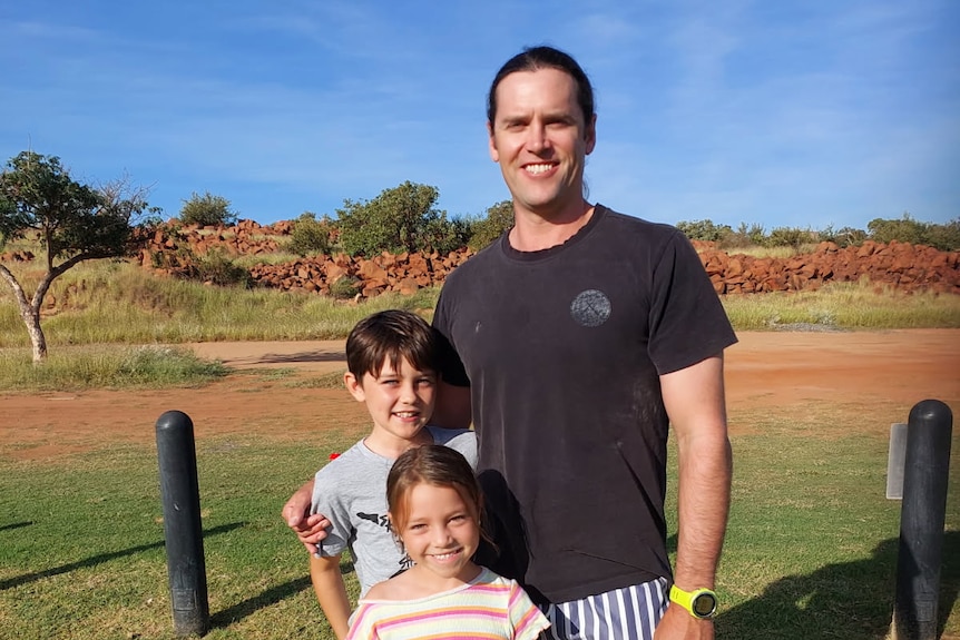 A smiling, dark-haired man and a little boy and girl stand in the sun.