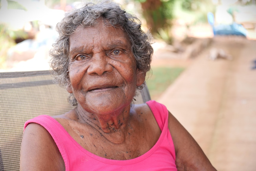 Woman in pink singlet sitting on porch chair outside looking at camera