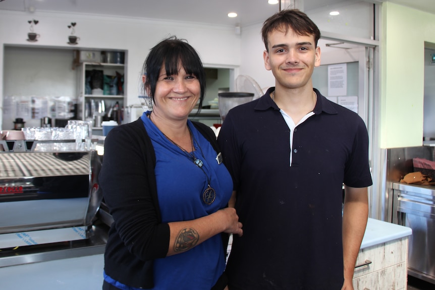 A woman and teenage boy smile while standing in front of a coffee machine