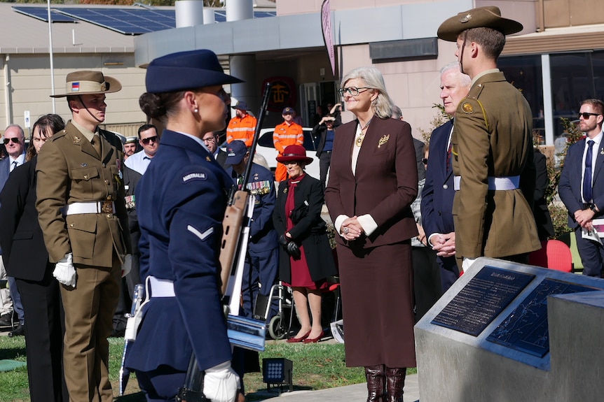 Woman in a brown suit surrounded by miltary members