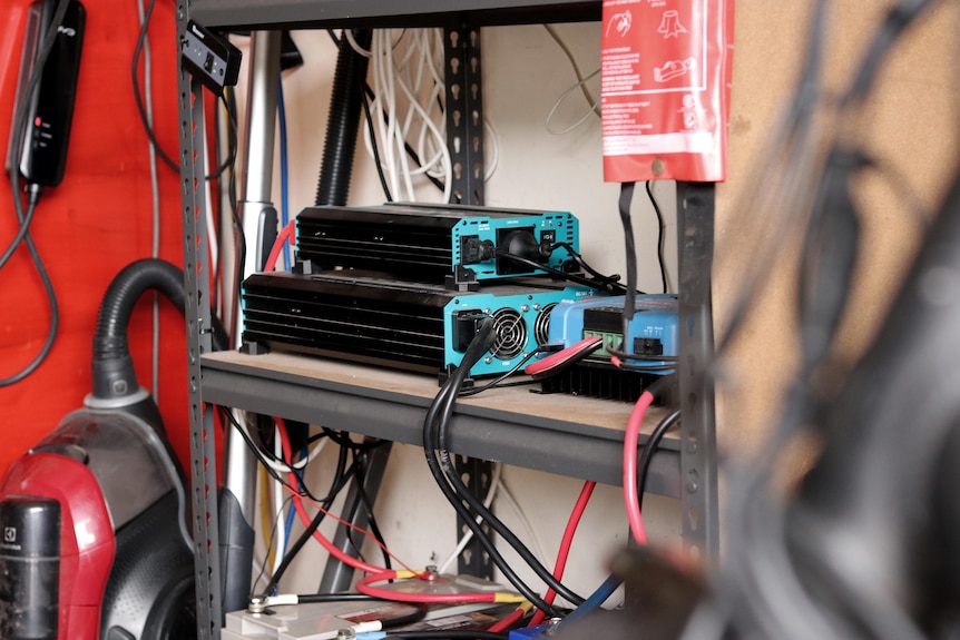 Two electrical boxes on shelving inside a garage with lots of cords going places.